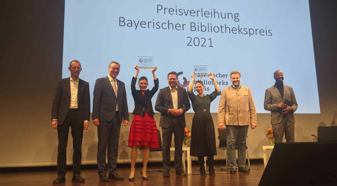 Die Preisverleihung (v.l.n.r.): Dr. D. Wintzer (StMWK), J. Götz (Bürgermeister Veitshöchh.), Dr. A. Wallat (Bücherei Veitshöchh.), Dr. G. Hopp (MdL, Vorsitz BBV), A. Hanke (Bücherei Gröbenz.), M. Schäfer (Bürgermeister Gröbenz.), Y. Dibaba (Moderator)